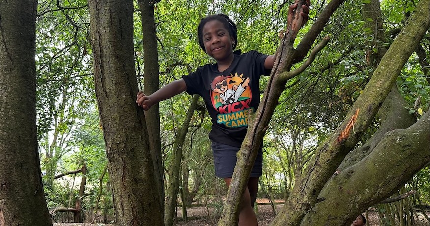 Child climbing a tree wearing a Kicx Academy summer camp t-shirt